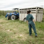 man in blue denim jeans standing beside blue tractor during daytime