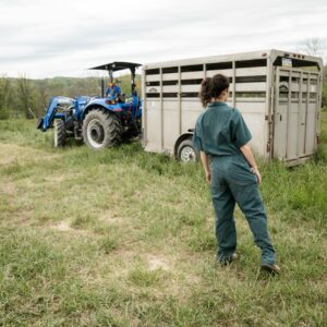 man in blue denim jeans standing beside blue tractor during daytime